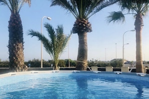 A swimming pool with palm trees and street lamps.