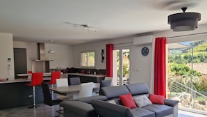 A modern living room with a grey sectional sofa, a dining area with red chairs, and a kitchen in the background.