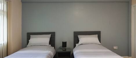 Habitación doble con dos camas, una mesita de noche con lámpara y una ventana con cortinas.