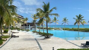 Zona de piscina en un resort, con palmeras, cielo despejado y vistas al océano.
