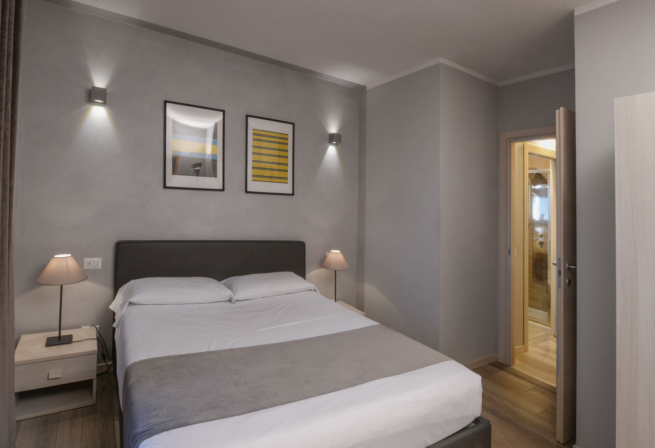 A modern bedroom with a bed, bedside lamps, and two framed artworks on the wall.
