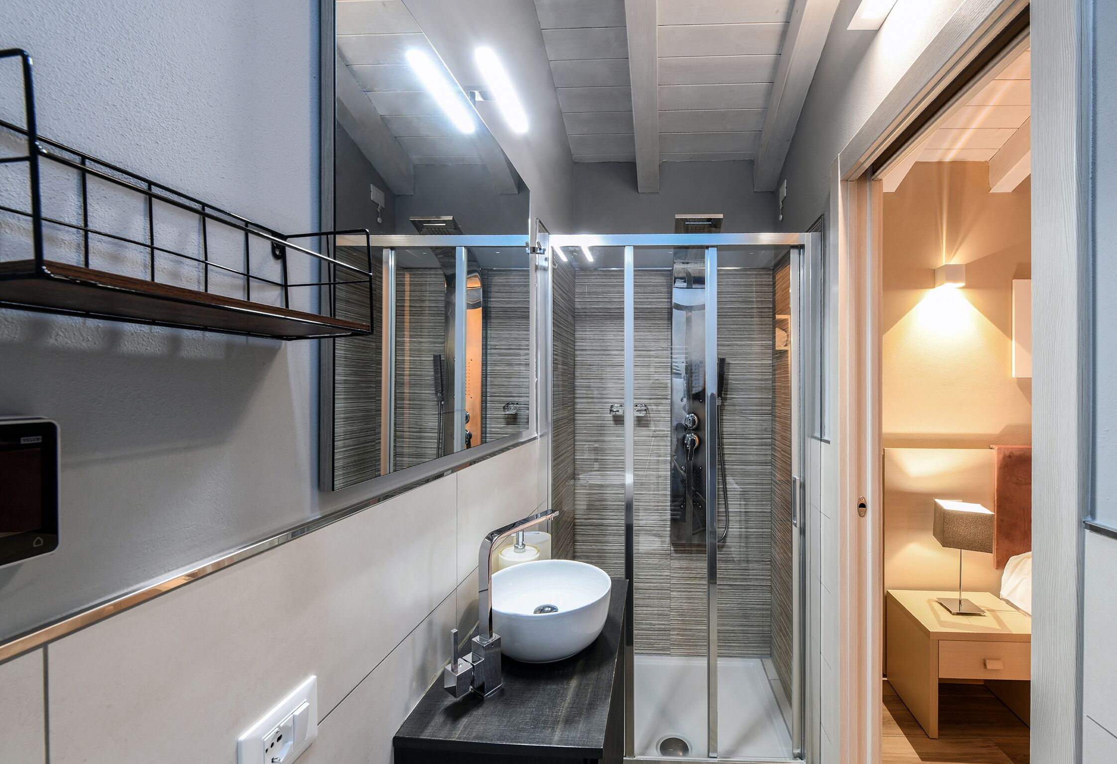 Un baño moderno con cabina de ducha de vidrio, un lavabo con recipiente y una mesita de noche con lámpara.