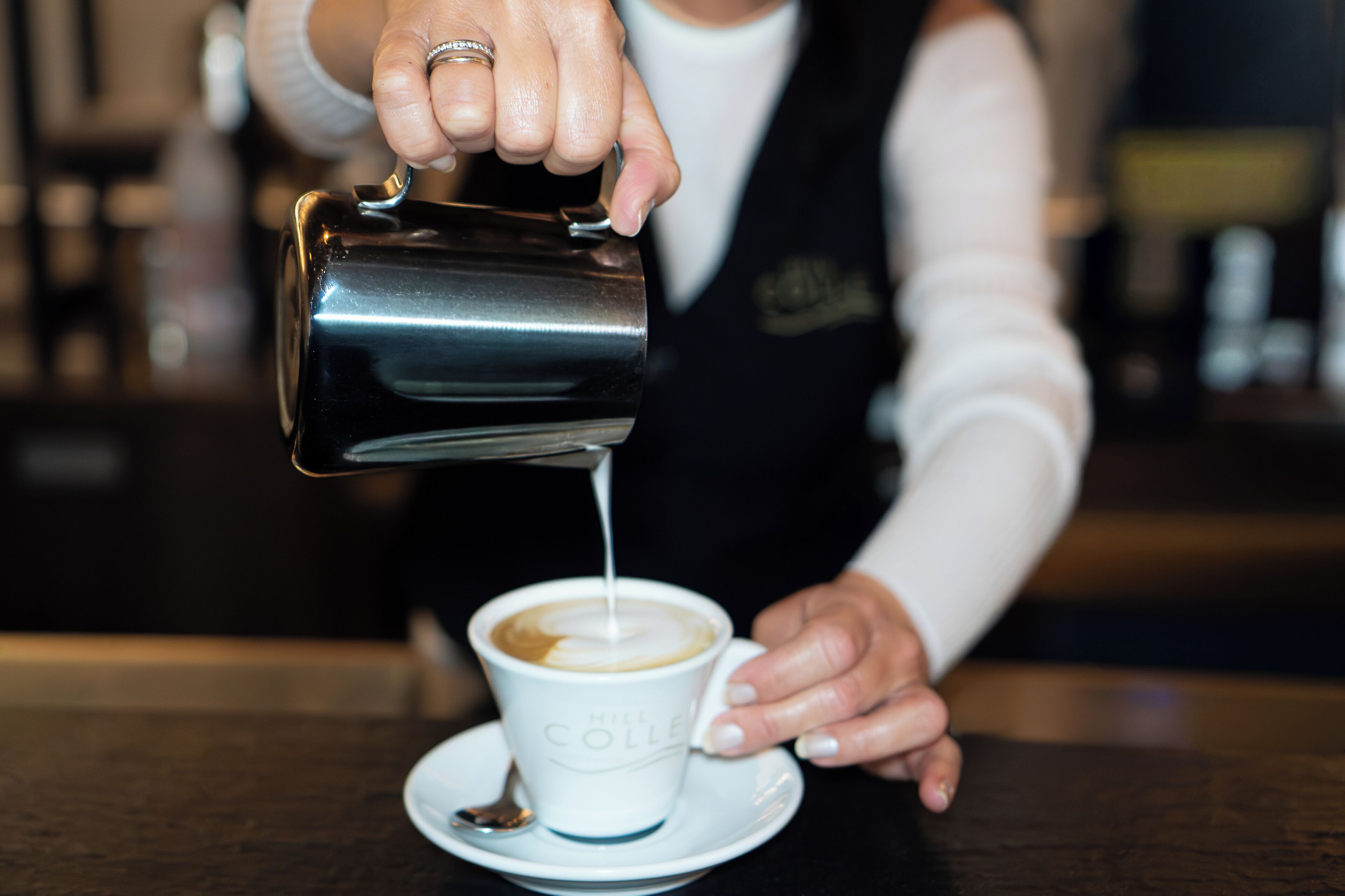 Alguém a verter leite para uma chávena de café.