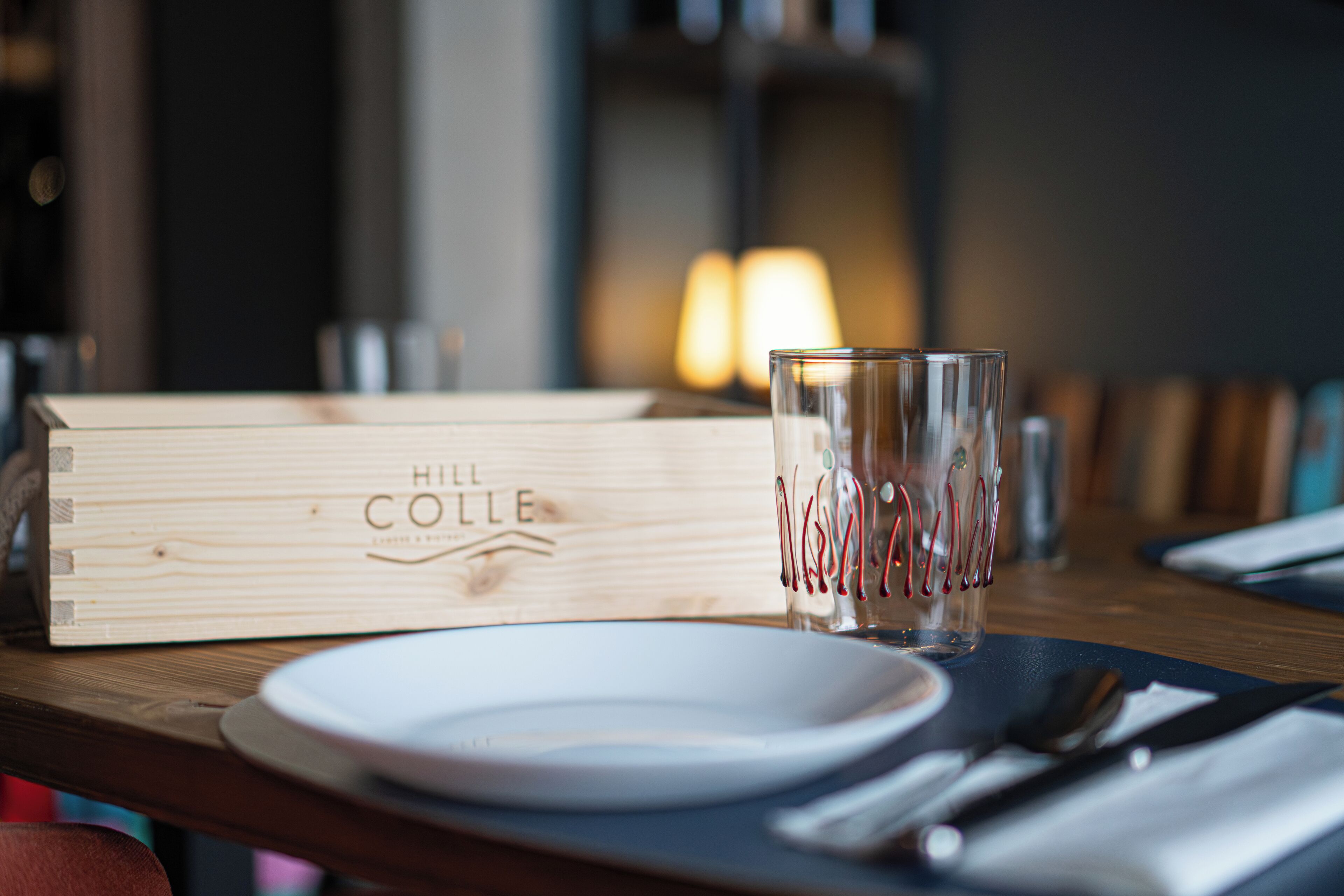 A wooden box labeled "Hill Collie" on a table with a glass, plate, and cutlery.