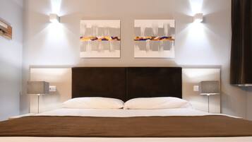 A modern hotel room with a large bed, two wall-mounted light fixtures, and abstract artwork above the bed.