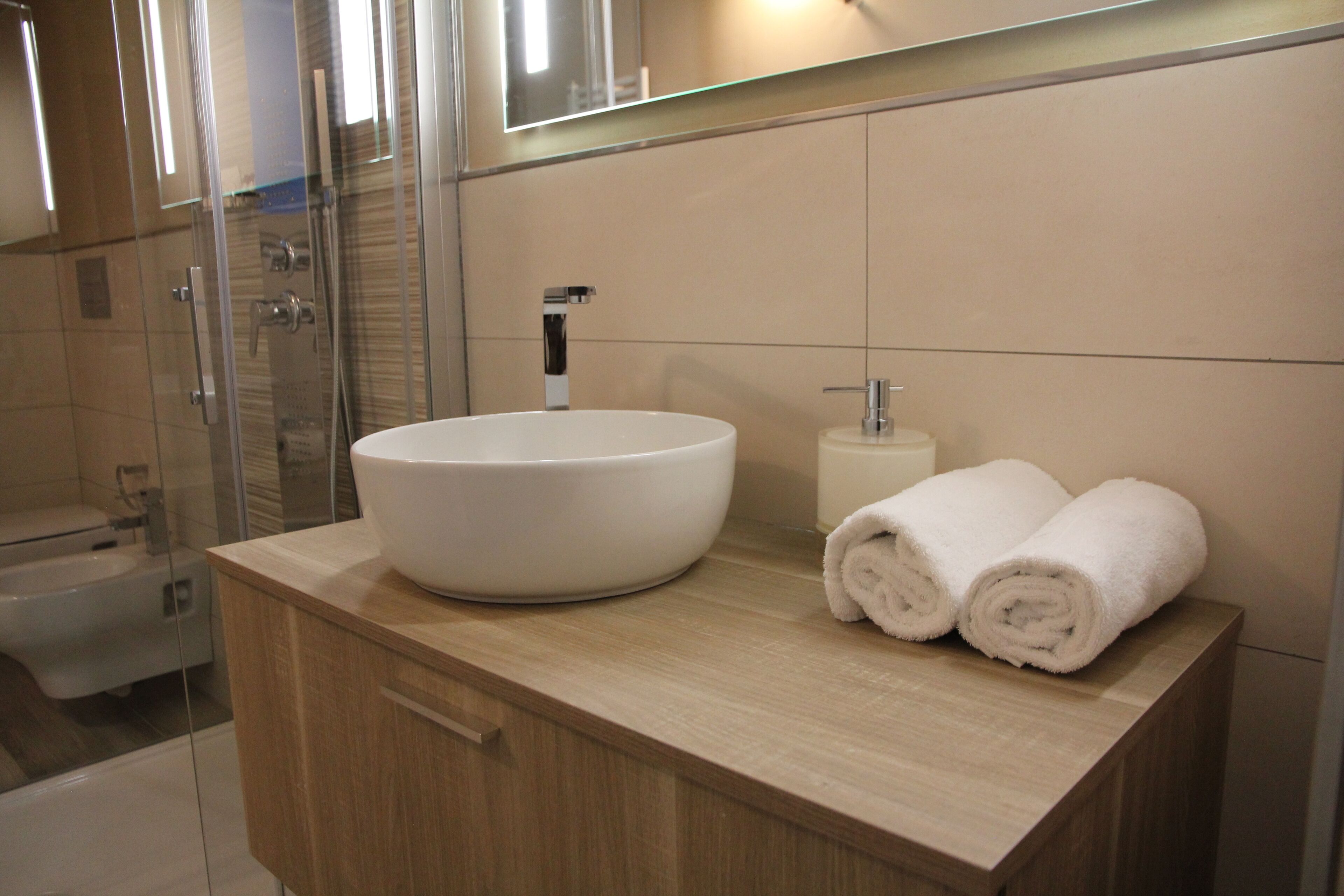 Une salle de bain moderne avec un grand lavabo blanc, une douche en verre et deux serviettes enroulées posées sur le comptoir.