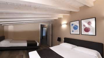 A hotel room with a large bed, a smaller bed, and a bench. There is a door leading to another room.