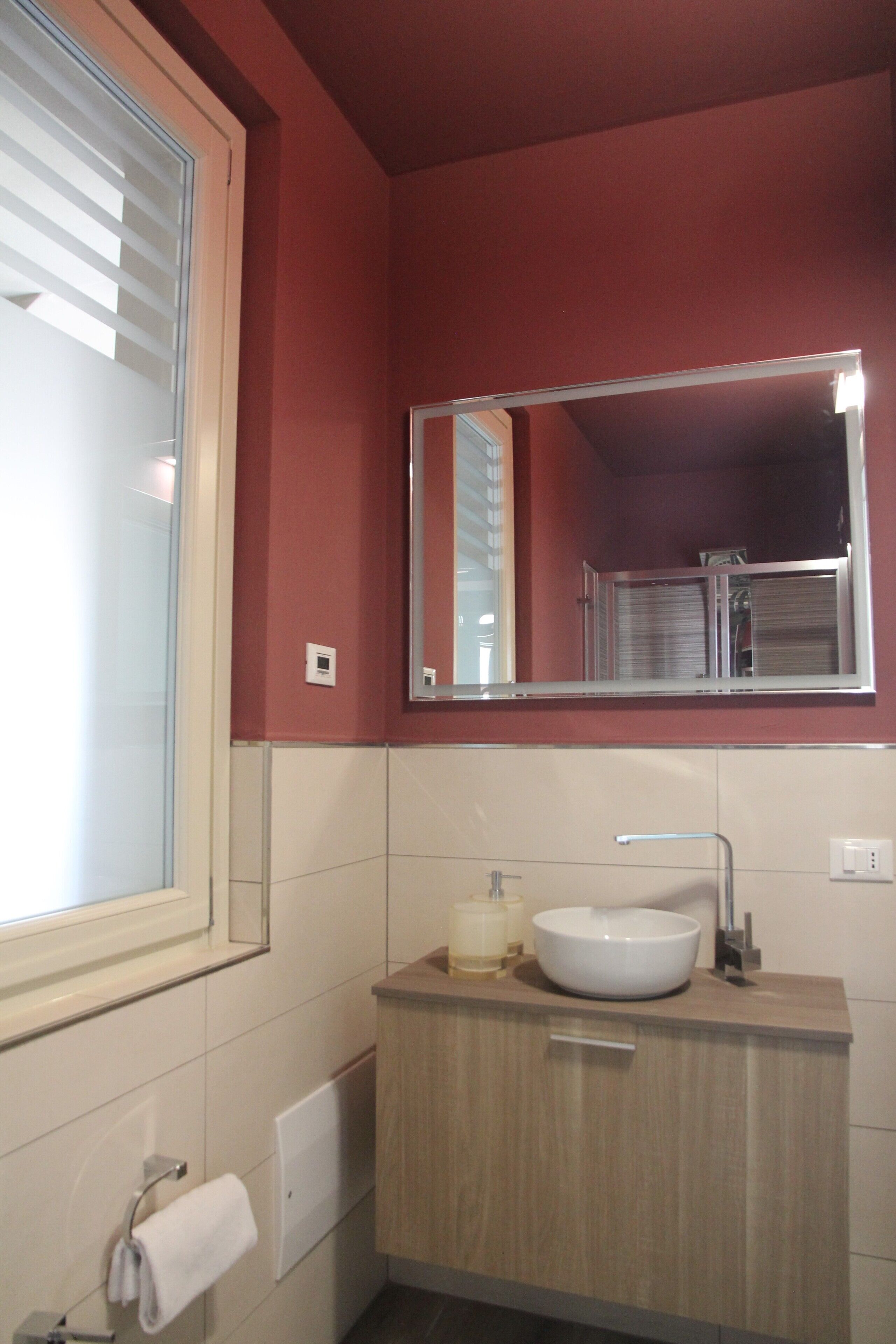 Un baño con lavamanos blanco, un espejo y una ventana con persianas.