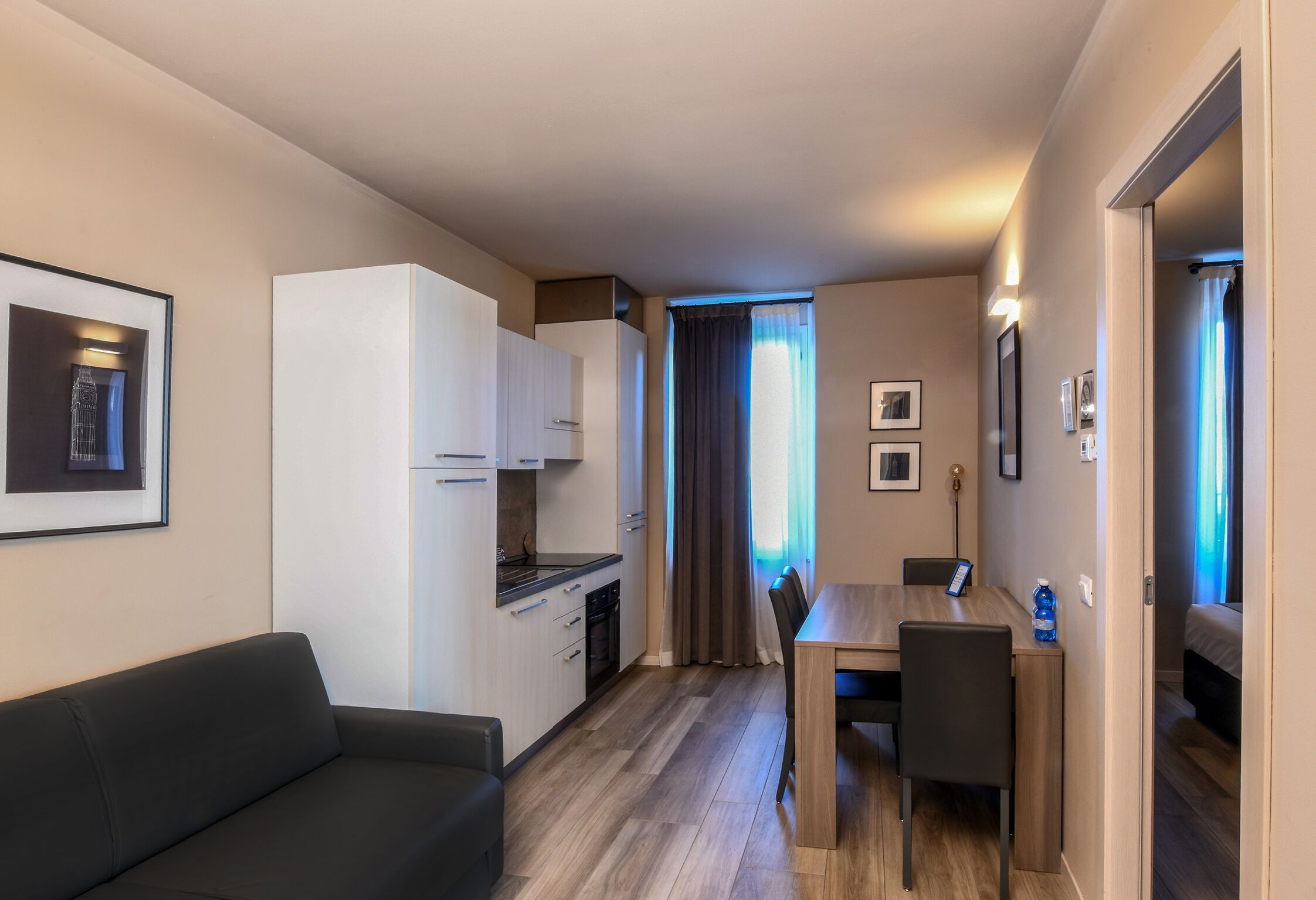 A compact hotel room with a kitchenette, a dining area, and a sofa.
