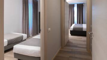 A hotel room with two beds, a wooden floor, and a view through an open door.