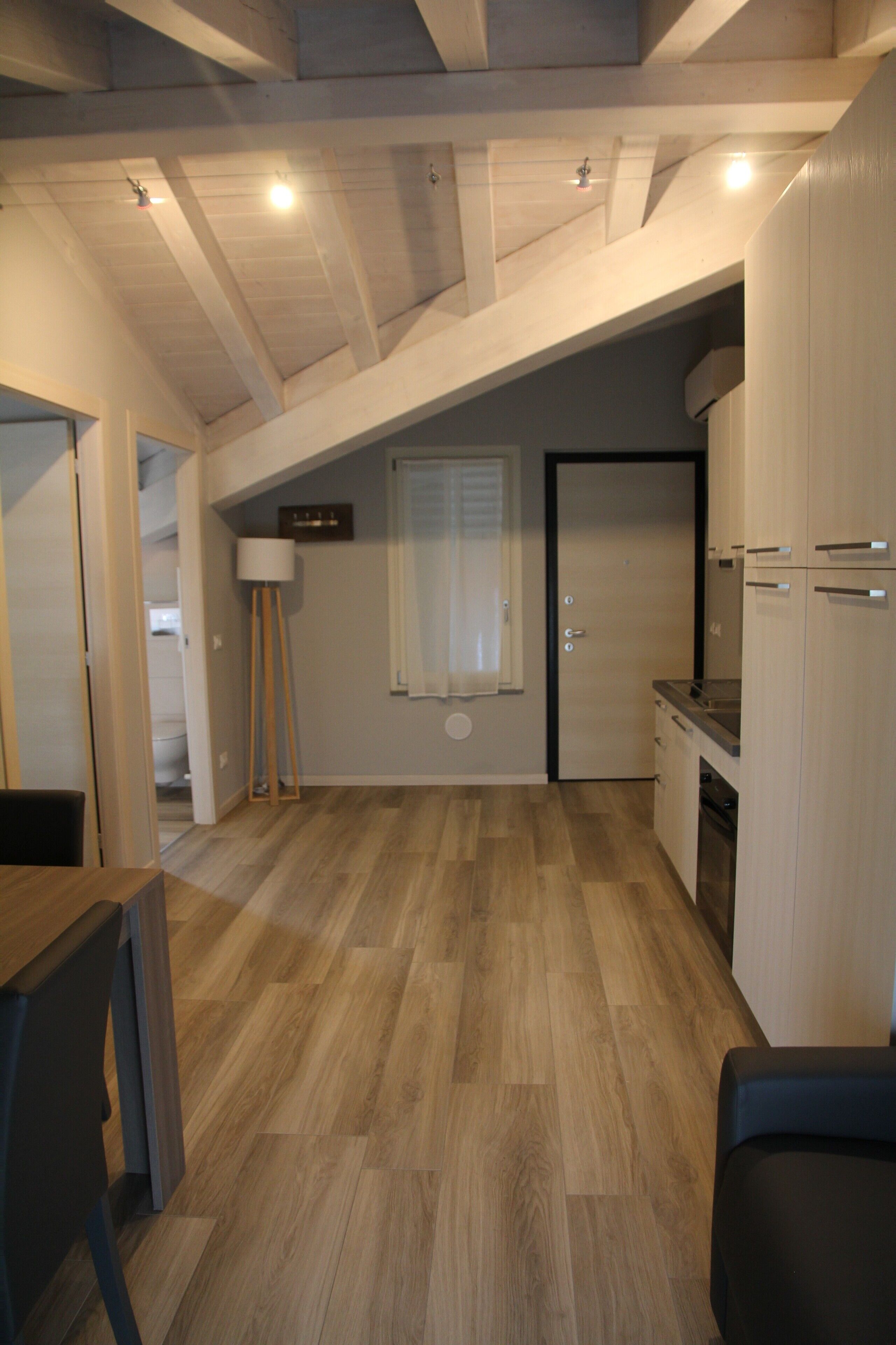 A kitchen with wooden flooring, a dining area with a table and chairs, and a ceiling with exposed beams.