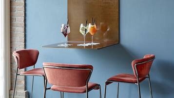 A dining area with a brick wall, a hanging light fixture, and three red chairs around a table with drinks.