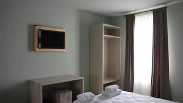 Una habitación de hotel con cama, mesita de noche, espejo, armario y ventana con cortinas.