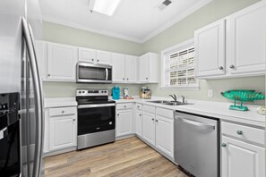 Une cuisine moderne avec des meubles blancs, des appareils en acier inoxydable et un plancher en bois.