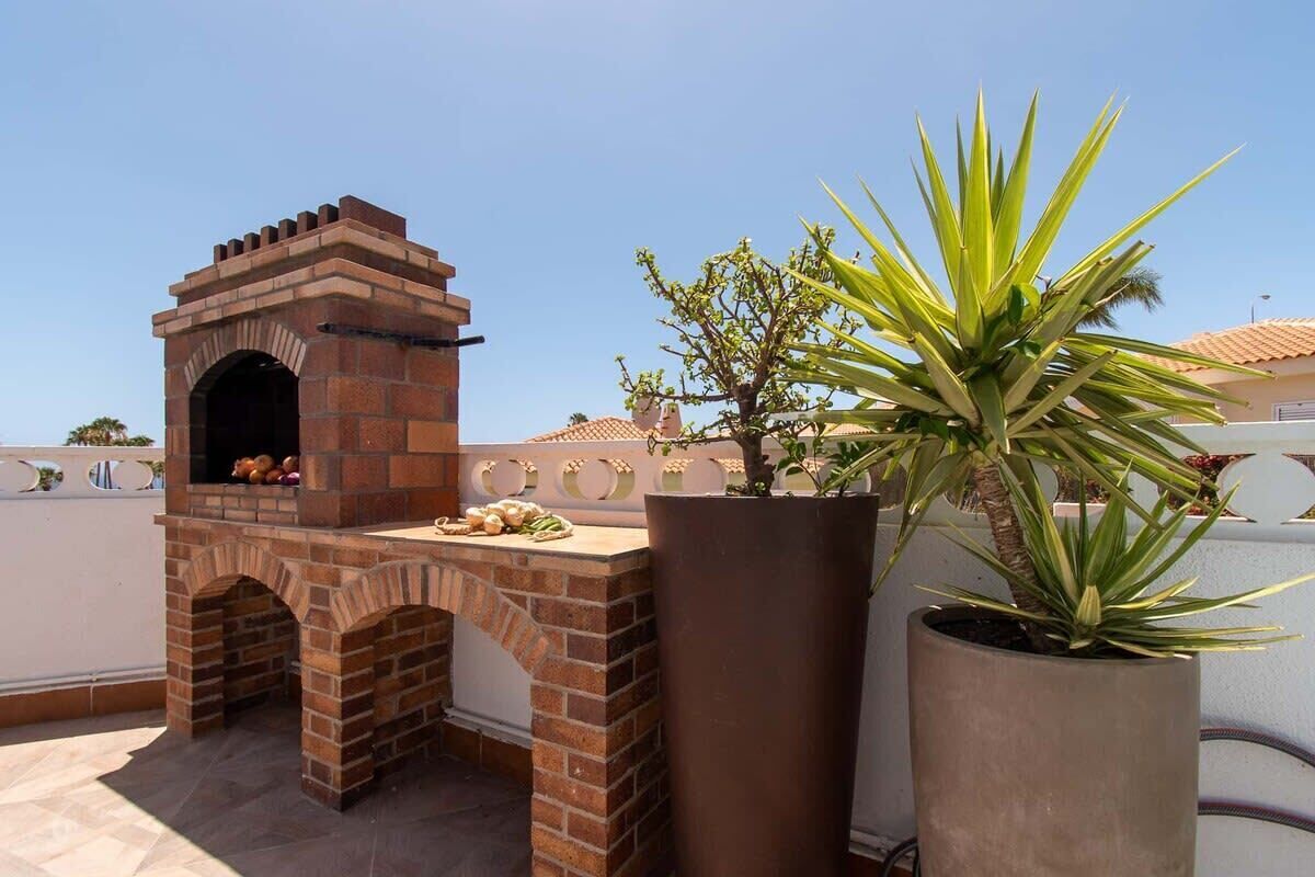A brick-built outdoor oven with a chimney, a potted agave plant, and a tiled patio area.