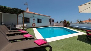 Ein Poolbereich mit Liegestühlen, einem Rettungsring und einem Gebäude mit einem Ziegeldach.