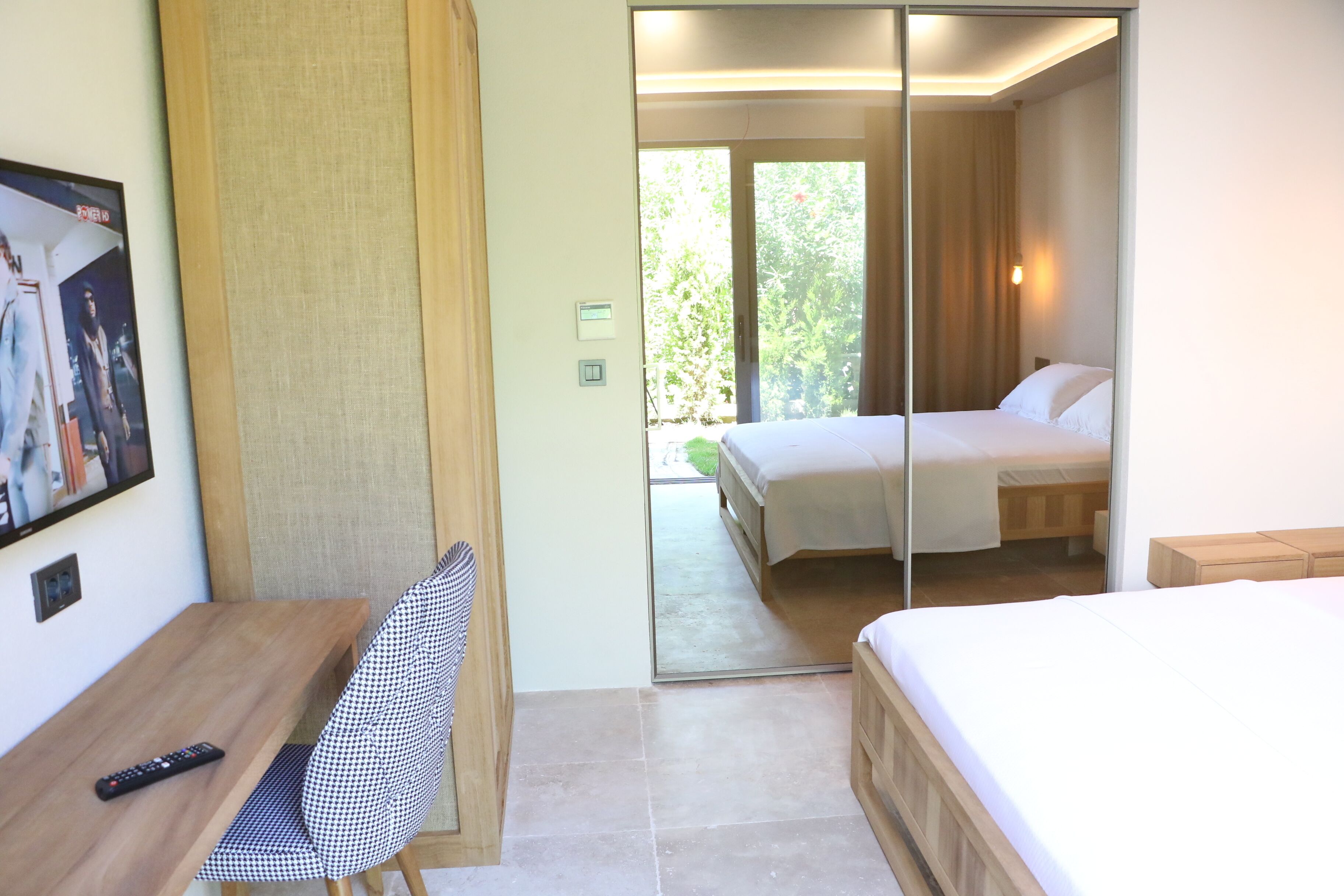 Habitación de hotel con cama, escritorio con silla, televisión y puerta corrediza que da a un balcón.