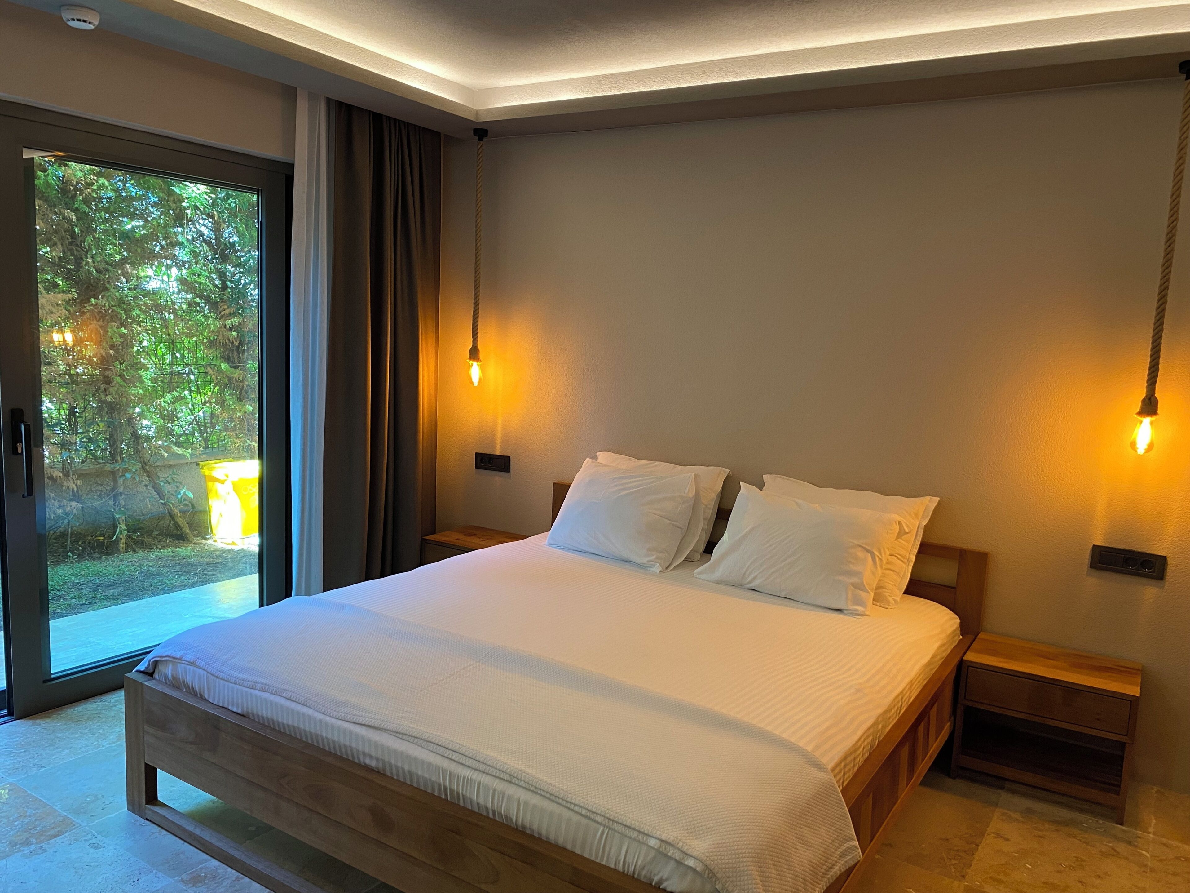 Quarto moderno com cama grande, mesas de cabeceira de madeira e iluminação ambiente.