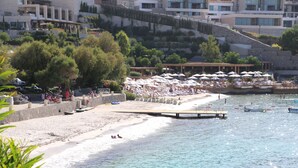 A beach with umbrellas and lounge chairs, a pier extending into the water, and buildings in the background. - Life Butiq Hotel (Bodrum)