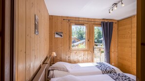 A wooden cabin bedroom with two beds, a window, and a lamp. - Apartment Rose des Alpes 2 for 6 people 4 **** (Samoëns)