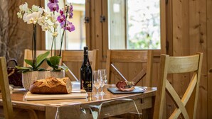 A wooden dining table with a loaf of bread, a bottle of wine, two wine glasses, a plate with food, and a potted plant with orchids. - Apartment Rose des Alpes 2 for 6 people 4 **** (Samoëns)