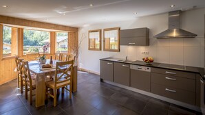 A modern kitchen with wooden cabinetry, a stainless steel range hood, and a dining area with a table and chairs.