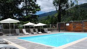 A rectangular swimming pool with a wooden deck, surrounded by lounge chairs and umbrellas.