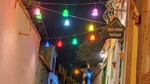 Una calle estrecha de noche con luces colgantes de colores y un cartel en idioma extranjero.