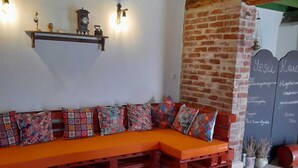 Un rincón acogedor con un banco de madera y cojines de colores, una pared de ladrillo y una pizarra con escritura.