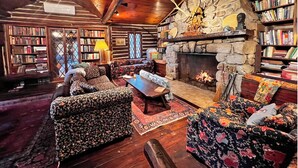Acogedor interior de una cabaña de madera con chimenea de piedra, estanterías y un espacio de estar confortable.
