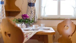Ein Holztisch mit einer blumigen Tischdecke, eine Vase mit lila Blumen und weiße Teetassen und Untertassen.