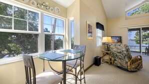 A room with a glass table and chairs, a sofa, and a view of trees through large windows. - Whitman Point Townhome Unit A is Gulf Front with Sunsets & fishing pier (Cedar Key)