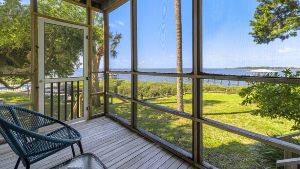 A covered outdoor area with a view of the sea, a wooden deck, and a chair. - Whitman Point Townhome Unit A is Gulf Front with Sunsets & fishing pier (Cedar Key)