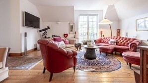 Un salon spacieux doté d’une grande fenêtre, d’un fauteuil en cuir rouge, d’un ensemble de canapés rouges, d’un télescope et d’un téléviseur à écran plat fixé au mur.