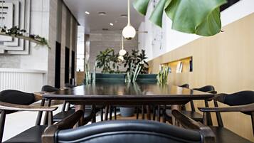 Un espace de salle à manger moderne, avec une longue table et des chaises noires, agrémenté de plantes et éclairé par des suspensions.