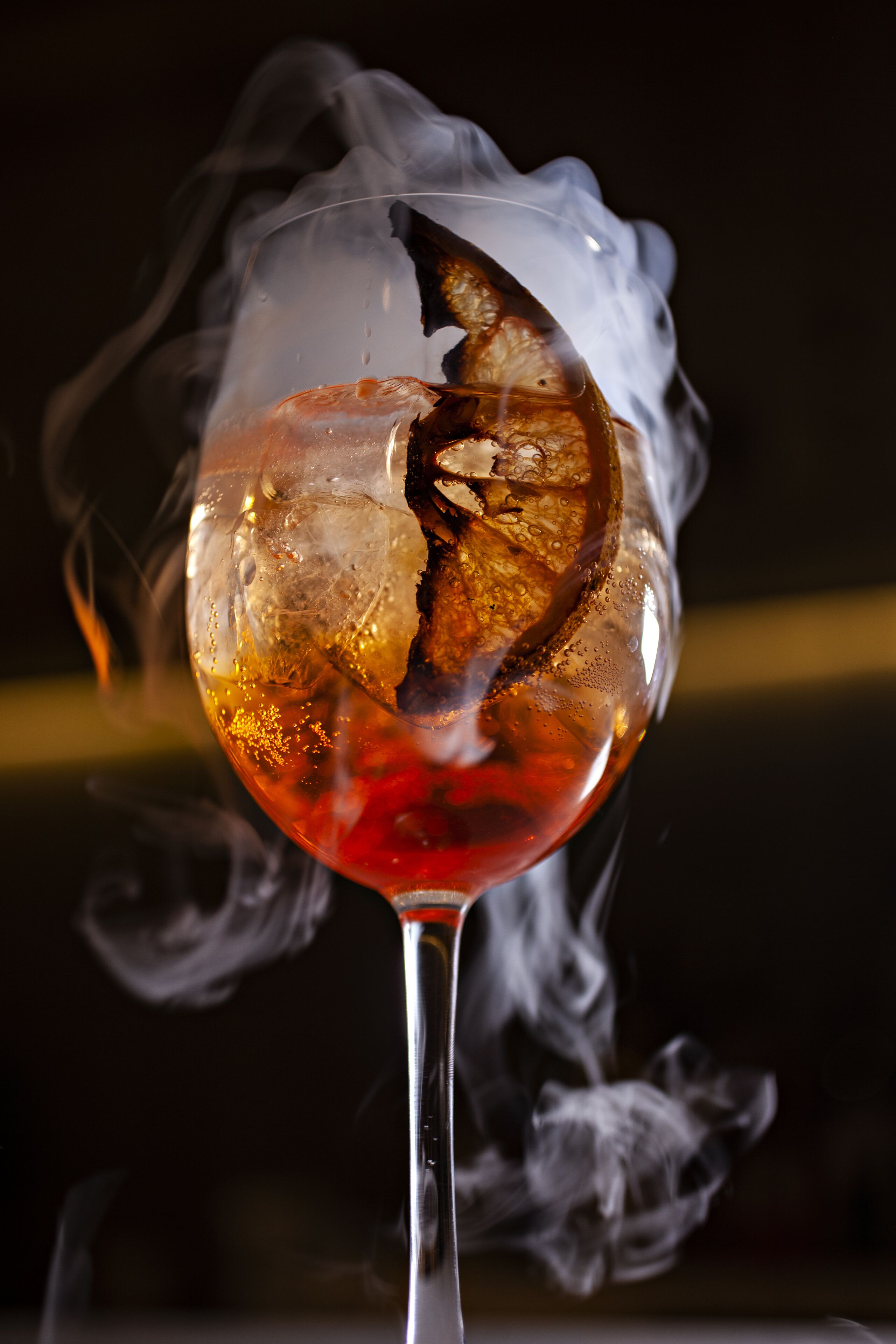 Un verre contenant un liquide rouge et des glaçons, entouré de fumée.