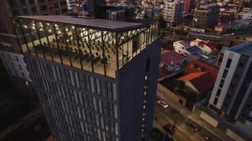 A high-rise building with a rooftop terrace featuring a glass enclosure and seating areas.