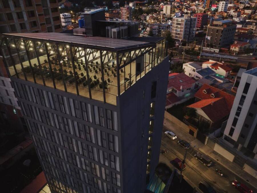 A high-rise building with a rooftop terrace featuring a glass enclosure and seating areas.