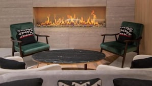 A modern living room with a fireplace, two green armchairs, a round coffee table, and patterned cushions. - MET Hotel (La Paz)