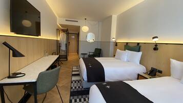 A hotel room with two beds, a desk, a chair, a TV, and a bathroom visible through an open door.