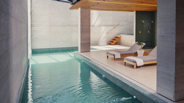 A modern indoor pool area with a clear pool, wooden deck, and lounge chairs. - MET Hotel (La Paz)