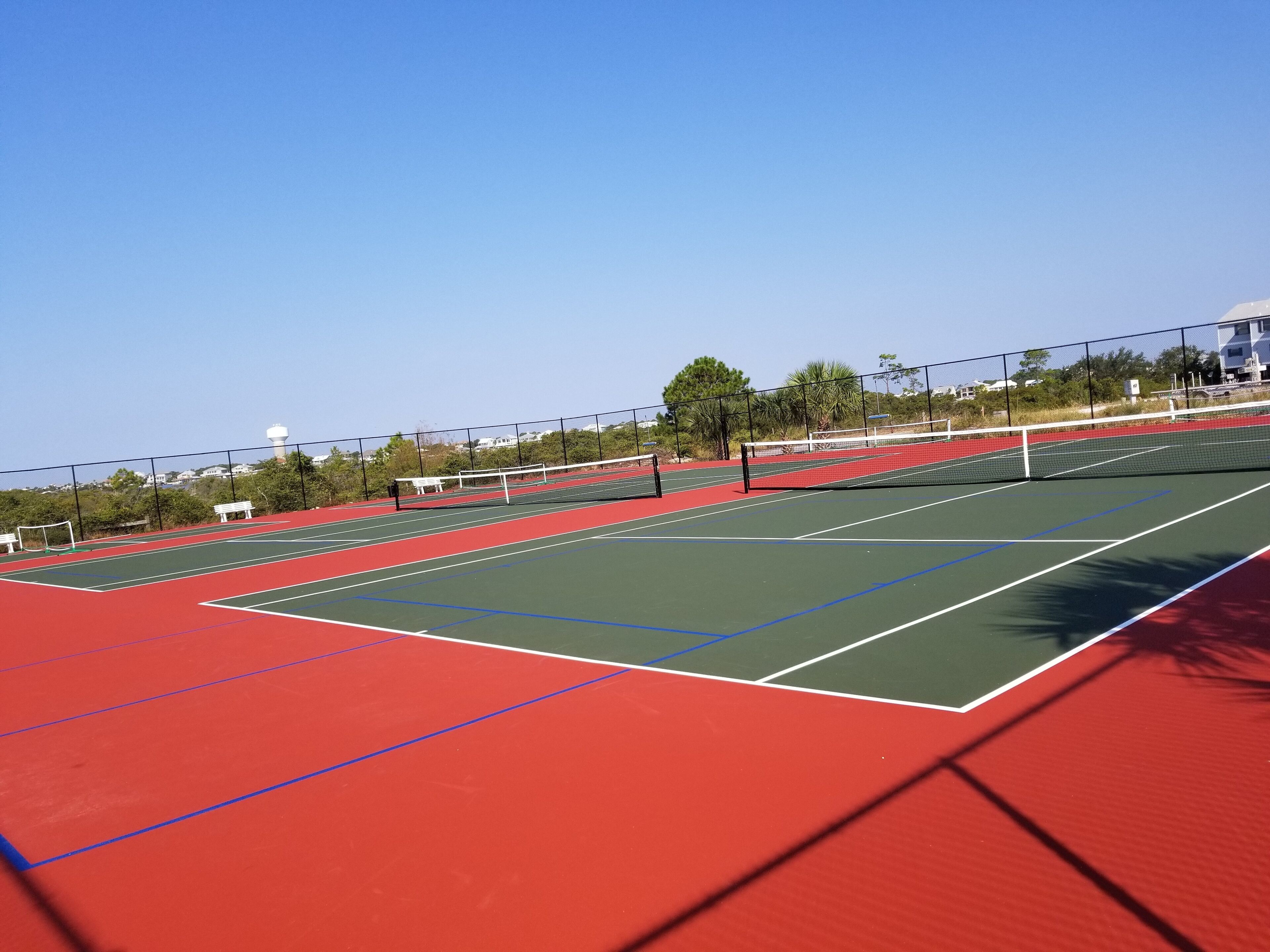 An outdoor tennis court with a net, surrounded by a fence and trees.