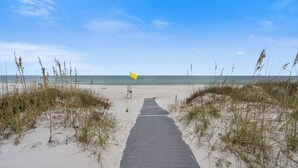 A sandy beach with a wooden boardwalk leading to the ocean, surrounded by grass. - Southern Peach East Beach House 3BD Private Pool Boat Dock (Pensacola)