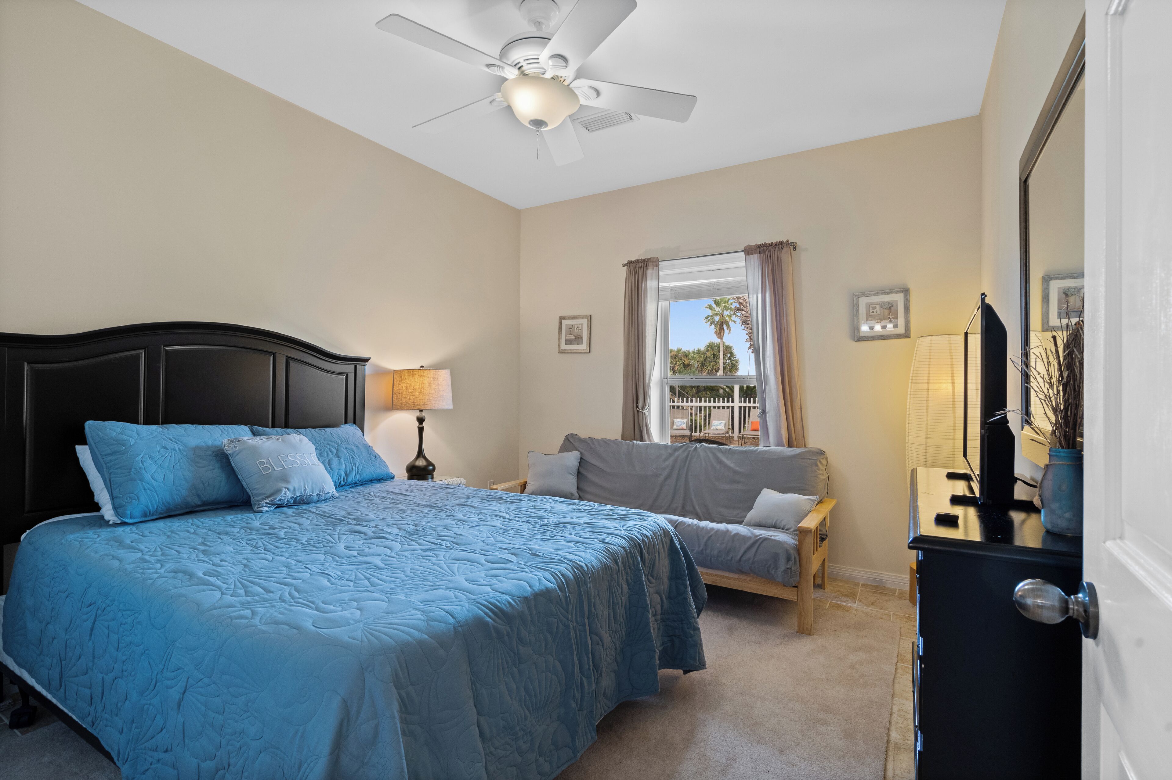A bedroom with a bed, a chair, a desk, a ceiling fan, and a window with curtains.