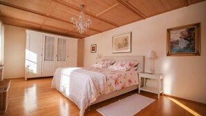 A bedroom with a wooden ceiling, a bed with floral bedding, a white bedside table, and a chandelier. - Ferienwohnung 1, 90 qm, Eigener Eingang, mit Terasse, 4 Sterne (Samerberg)