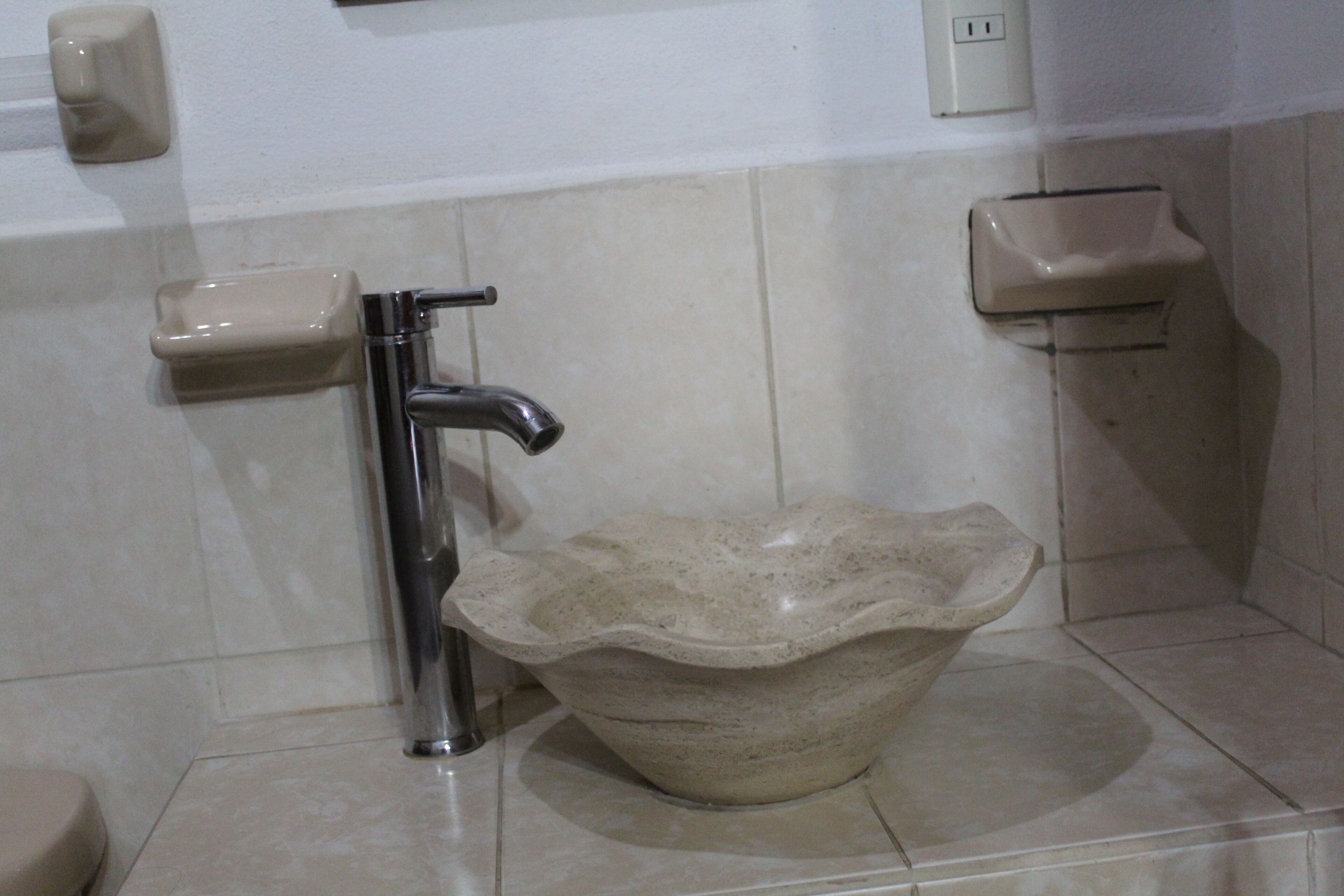 A bathroom with a modern sink, a faucet, and a soap dispenser on the wall.