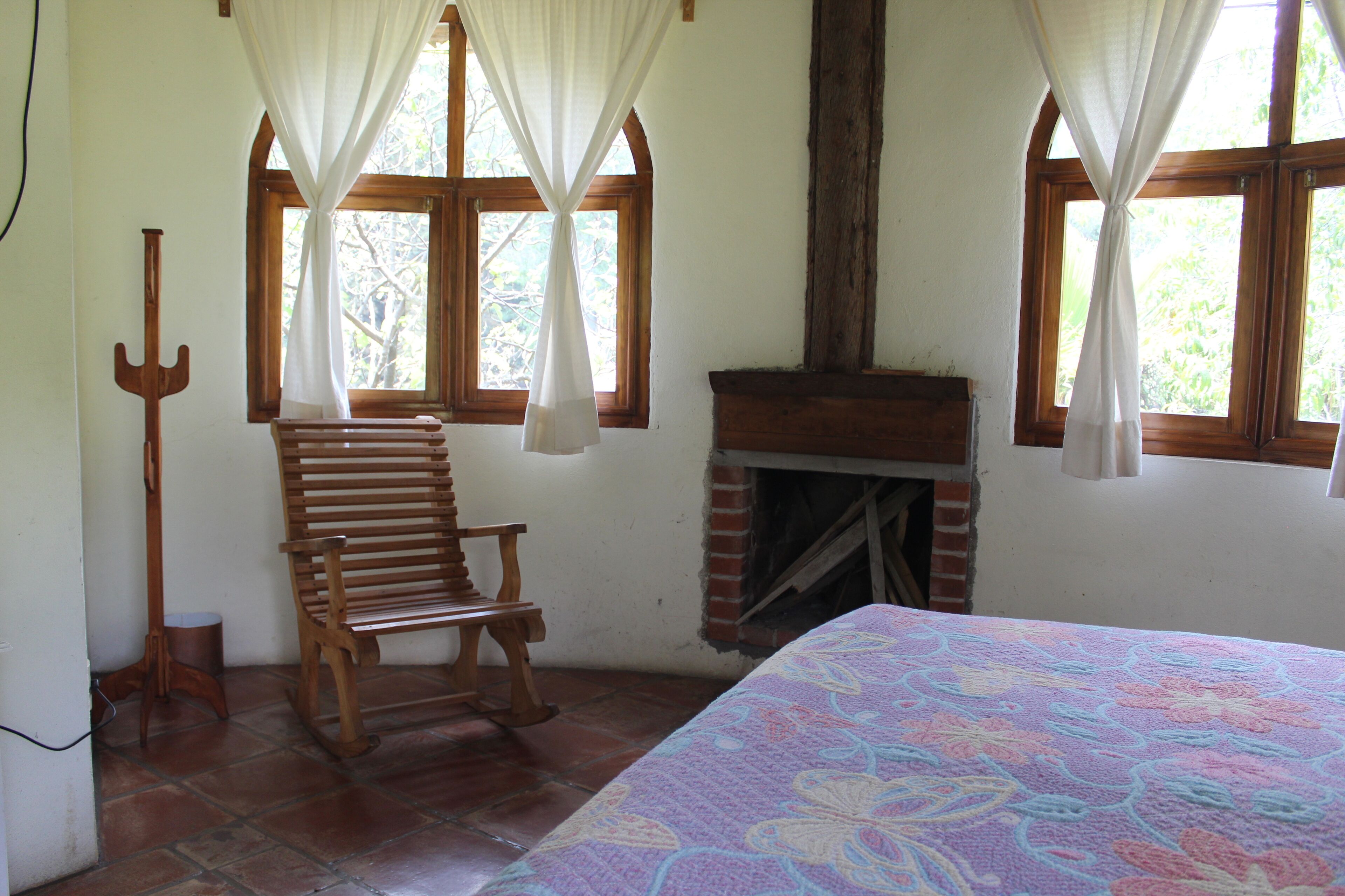 A room with a wooden chair, a fireplace, and a bed with a floral-patterned bedspread.