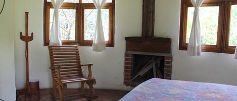 A room with a wooden chair, a fireplace, and a bed with a floral-patterned bedspread.
