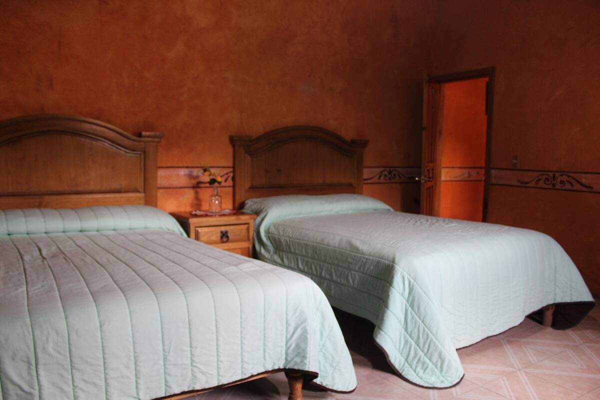 A bedroom with two beds, wooden headboards, a nightstand with a lamp, and a door.