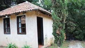 A small building with a tiled roof and two windows, surrounded by greenery and a stone pathway. - Cabañas Esperanza (Tlalpujahua)
